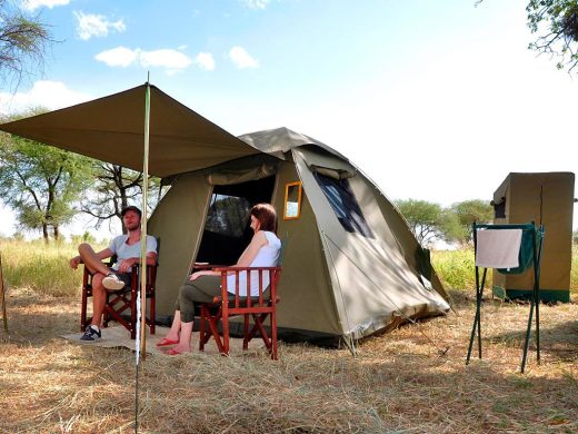 Couple relaxing outside a budget safari tent in the African savanna during a camping safari
