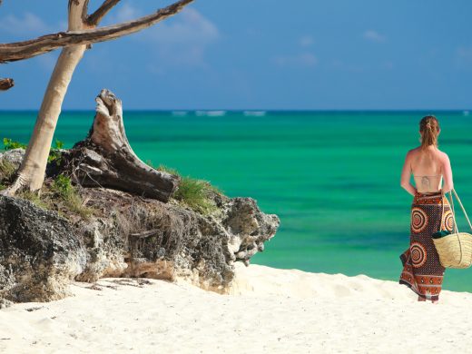 Woman walking along a pristine white-sand beach with turquoise ocean waters in Zanzibar, Tanzania.