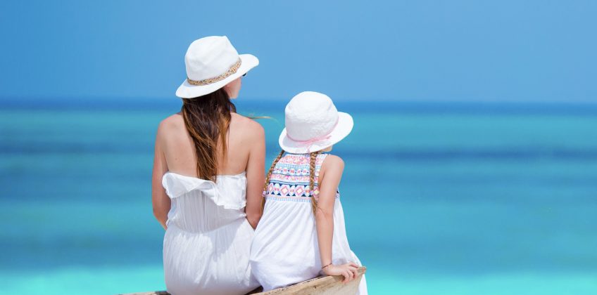 5 Days Discover Zanzibar Luxury Beach Holiday A mother and daughter sitting on a rustic wooden boat on a stunning white sand beach, looking out at the bright turquoise ocean.